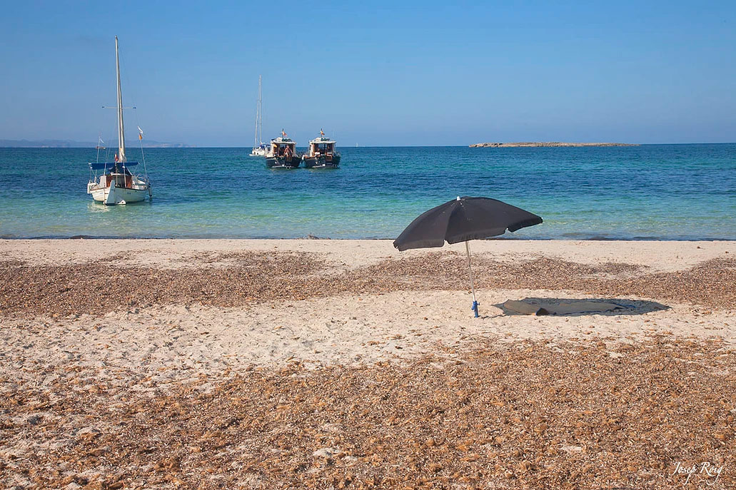 Playa de Es Carbó con sombrilla en la orilla y barcos tradicionales